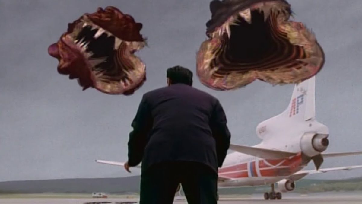 A man in a black suit seen from behind staring at two circle teeth monsters on The Langoliers